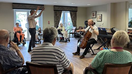 A cellist and a violinist perform for a small group of people in a comfortable, intimate setting.