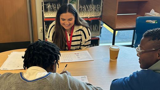 Student working with tutor. Sat around a table.