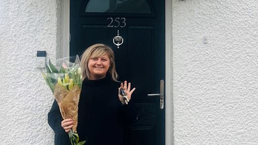 Ms.May stood at the door of her home holding a bouquet of flowers and keys