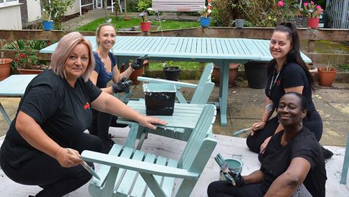 Four Axis volunteers painting garden furniture with teal blue.